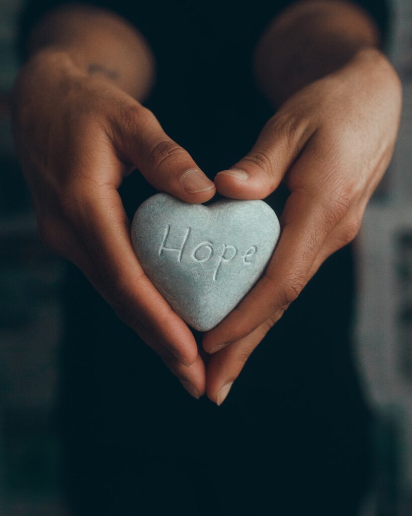 Woman holding heart-shaped stone with "hope" written on it